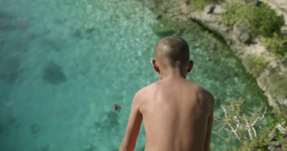 A boy jumps off a cliff and joins his friends in the sea