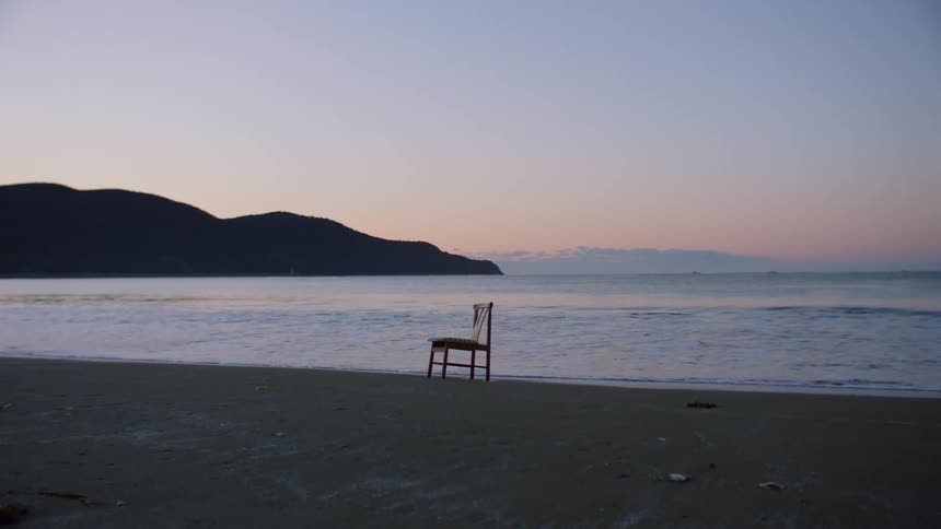 A chair is sitting on a beach as waves roll into shore and stop right where the legs are in the sand