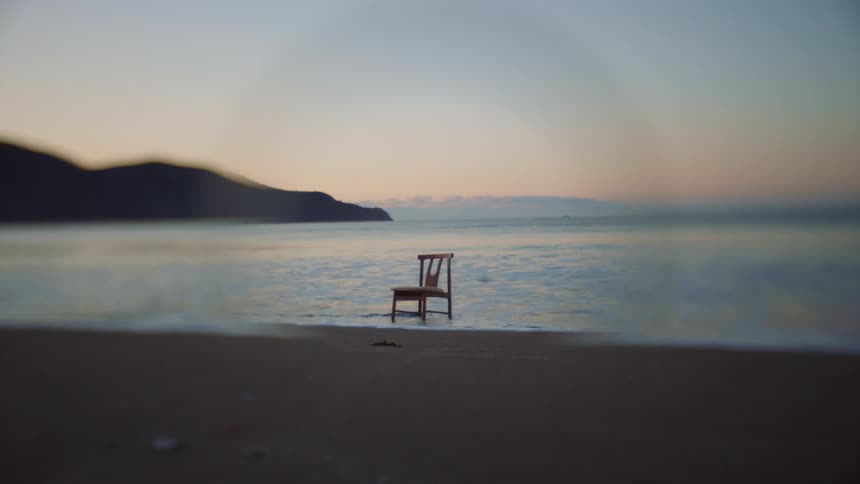 A chair is sitting on a beach as waves splash and roll into shore and under its legs on the sand