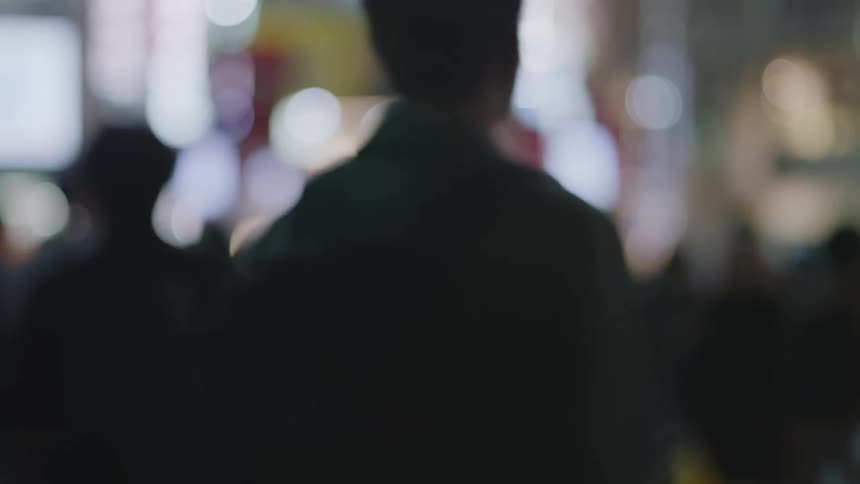 A crowd of people walk throughout a busy area of a city at night