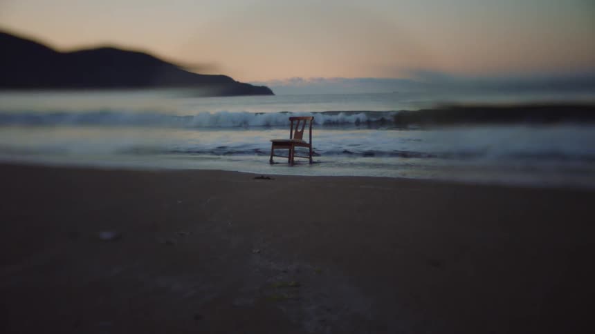 Wooden chair stands on the beach next to the sea at sunset