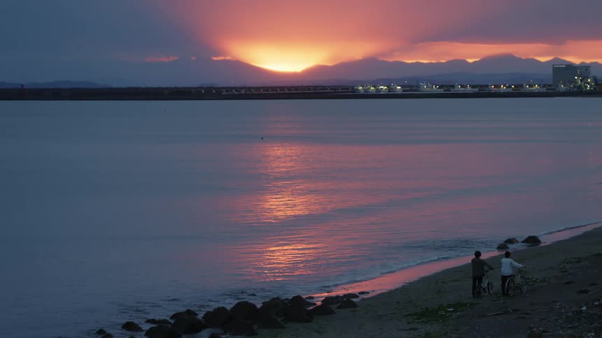 Two people watching a sunset on a sandy beach