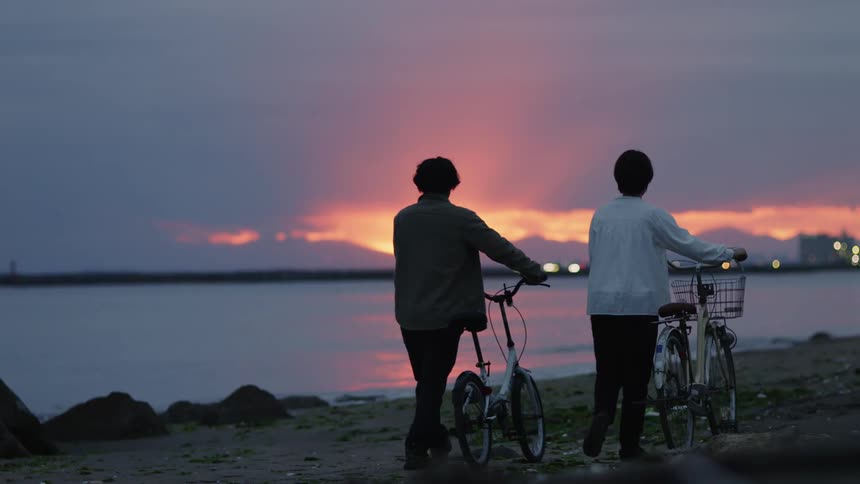 Two people push their bikes on the beach