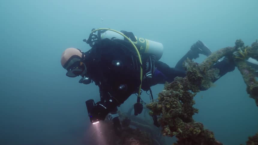 A scuba diver is swimming with a flashlight exploring the ruins of a sunken ship