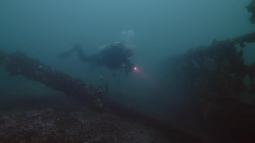 A diver uses a flashlight to examine wreckage on the sea floor