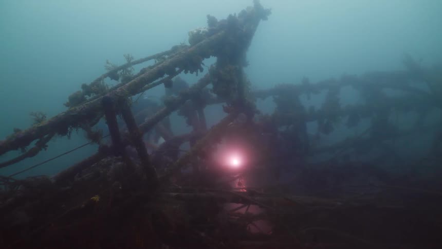 A couple of scuba divers shine a light on the remains of a shipwreck underwater