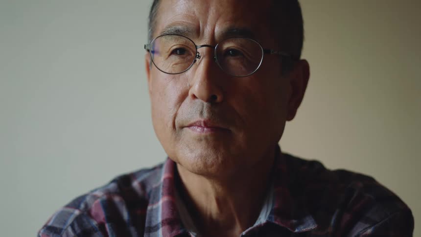 Older man wearing glasses sits and looks around a bit