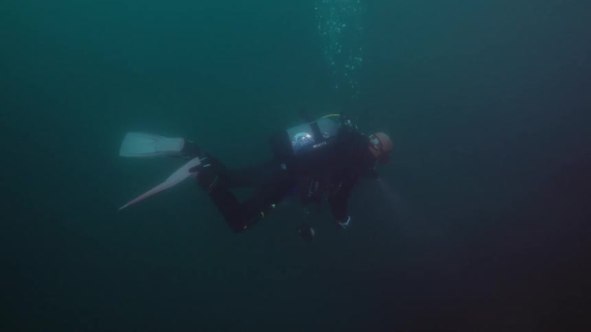 Scuba diver with wetsuit tan and flippers swims underwater