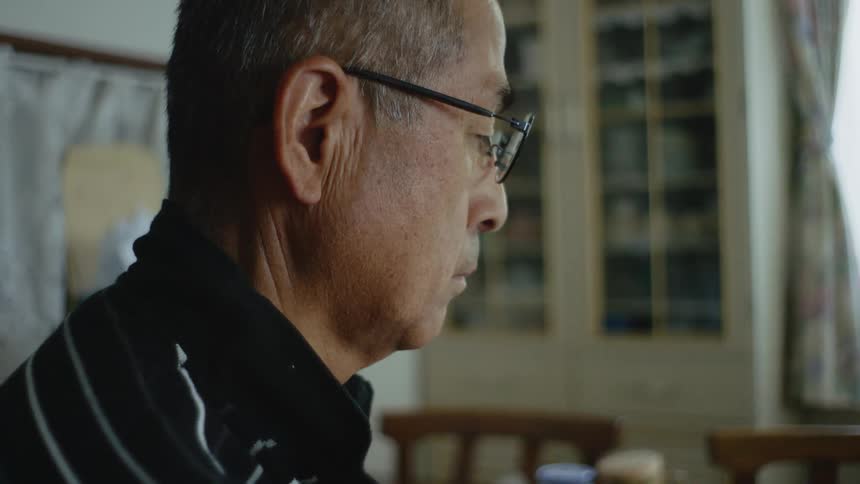 An older man is sitting down inside of his house