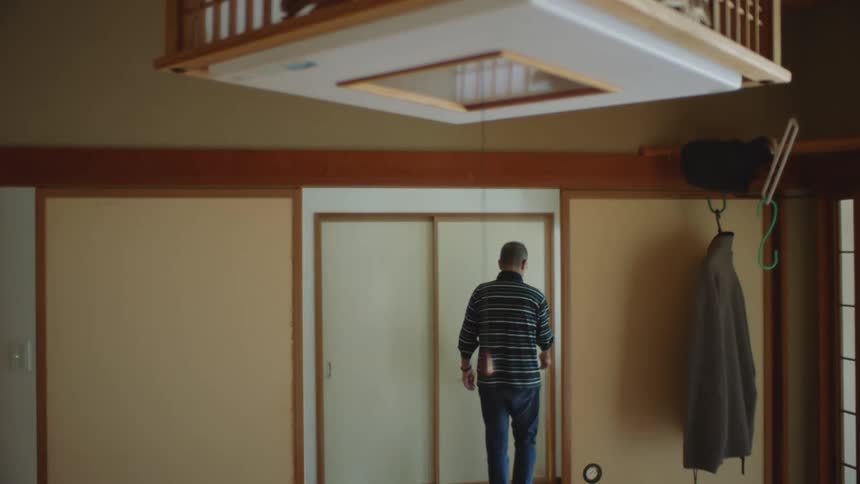 An older man is walking inside of his house in the day time