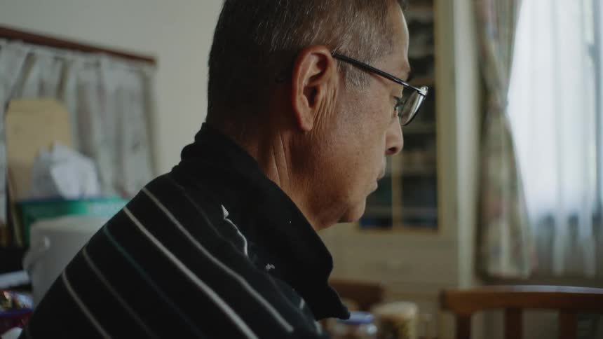 A man is sitting indoors at a kitchen table