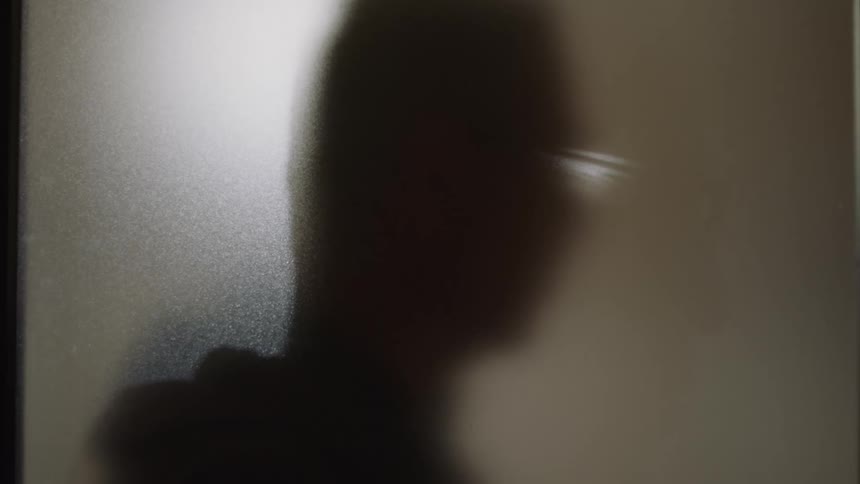 A man nods his head while standing near a frosted window
