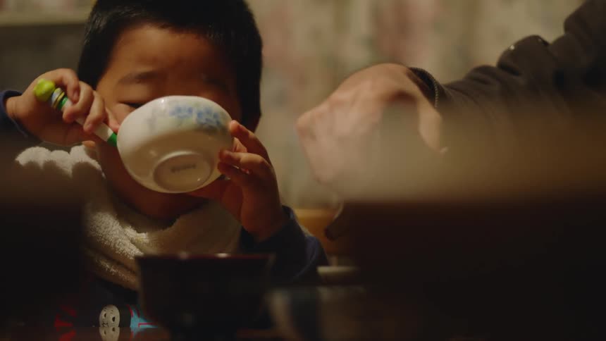 Adult seasons food while young boy eats happily