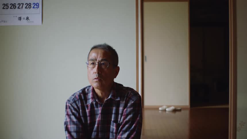 An older man is sitting down inside of his bedroom