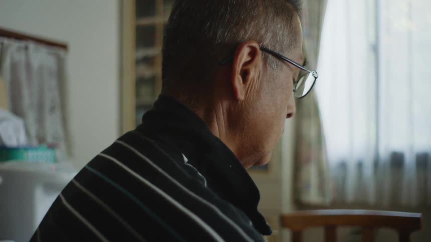 An older man is sitting down inside of his bedroom