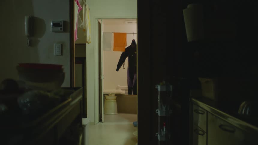 Person adjusts outfit hanging on shower rod in bathroom across hallway from kitchen