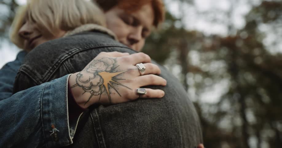 Tattooed woman gently hugging her partner in the park at evening