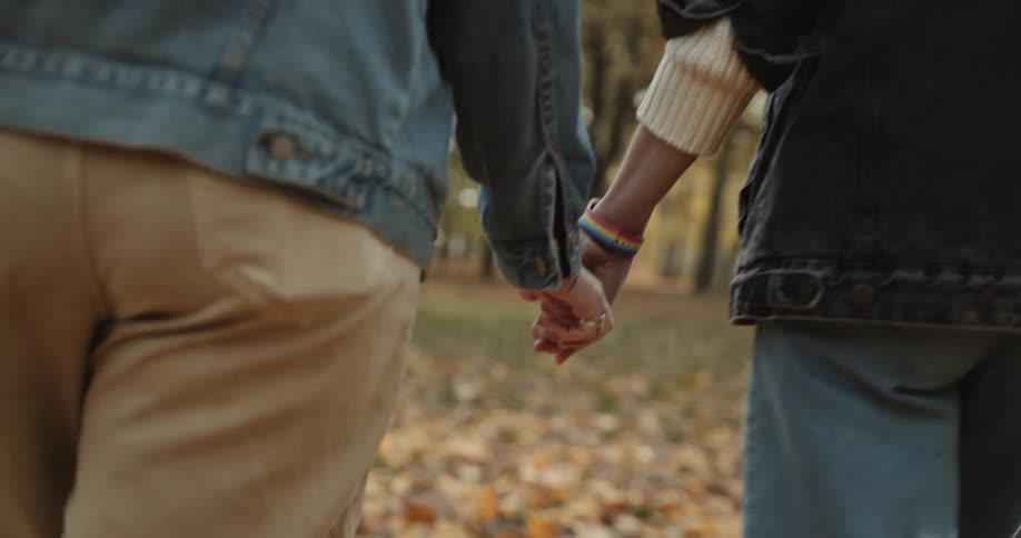 Lesbian couple wearing denim jackets and pants walks in the public park with brown leaves