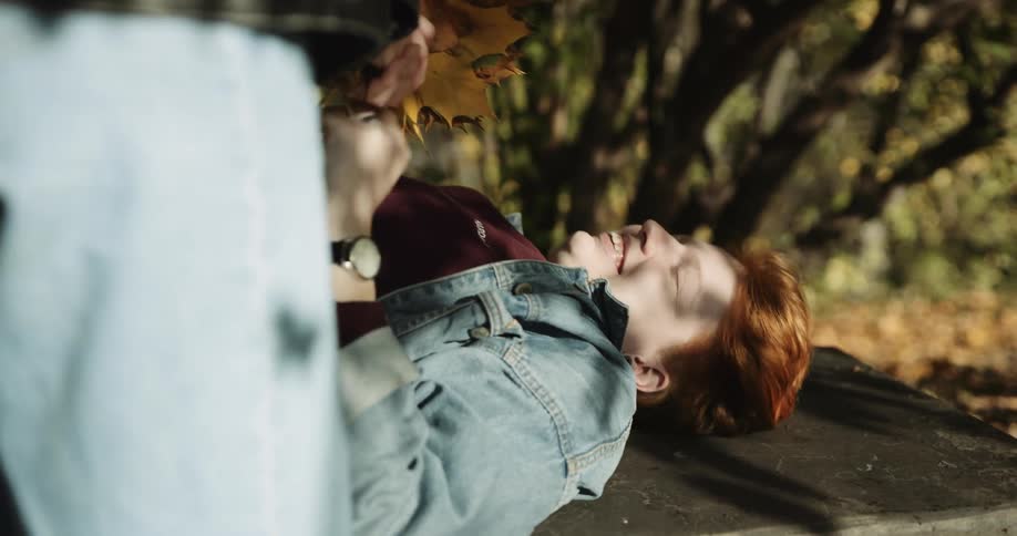Young woman brings a bunch of autumn leaves as a gift to her girlfriend resting on a bench