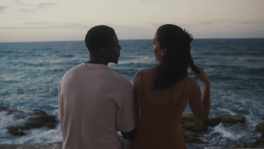 Young couple sitting on the beach in front of the ocean at evening