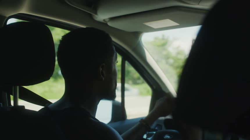 Young man talking to a passenger while driving a car at daytime