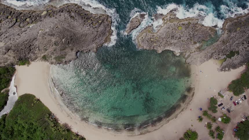 A circular ocean cove with turquoise water lies behind large rock berms