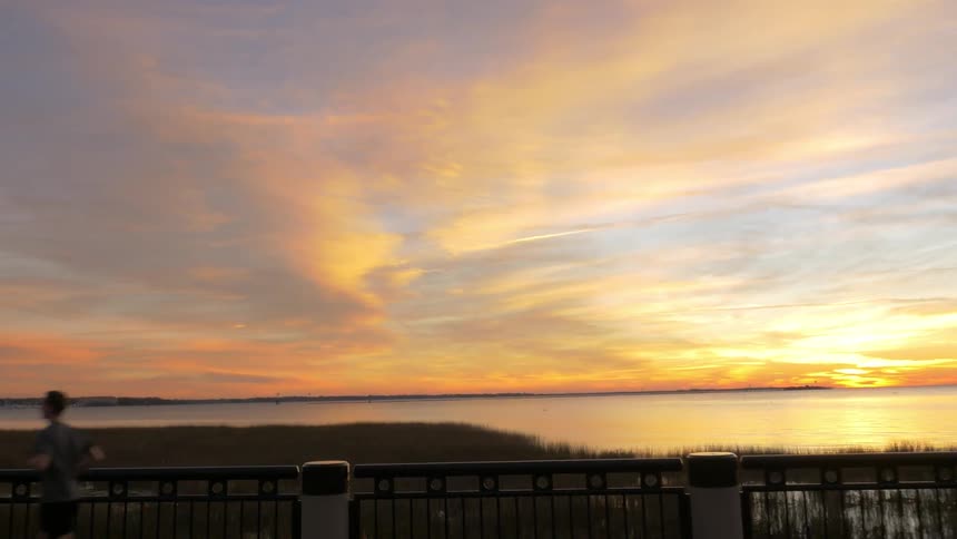 A man runs along the boardwalk by the shore at sunset