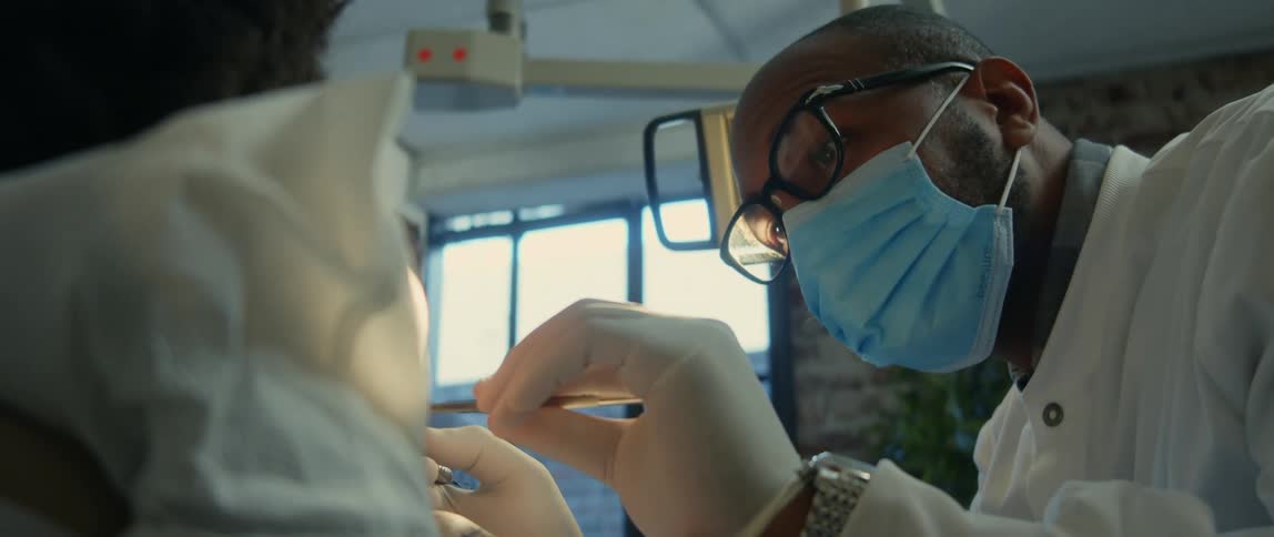 Dentist wearing a blue face mask checks the mouth of a patient