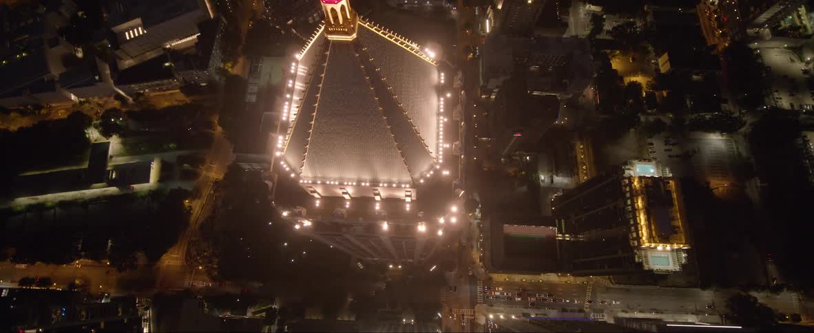 Orbiting aerial view of the illuminated top of a tall skyscraper in the city at night