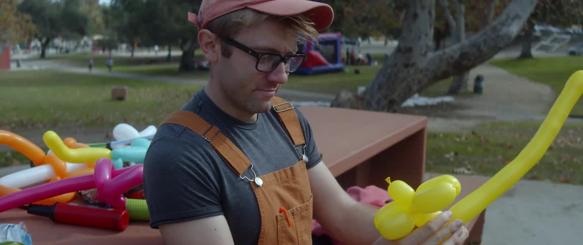 Male balloon artist sitting on a bench in a park making balloon animals