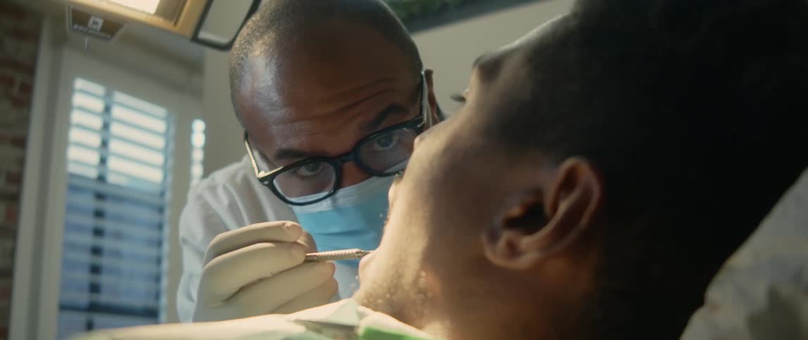 A man lies in a chair as a dentist looks in his mouth