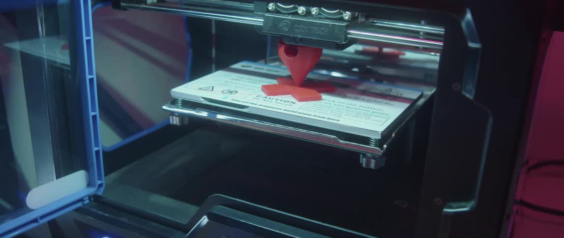 Close up of a 3d printer printing a model made of red plastic