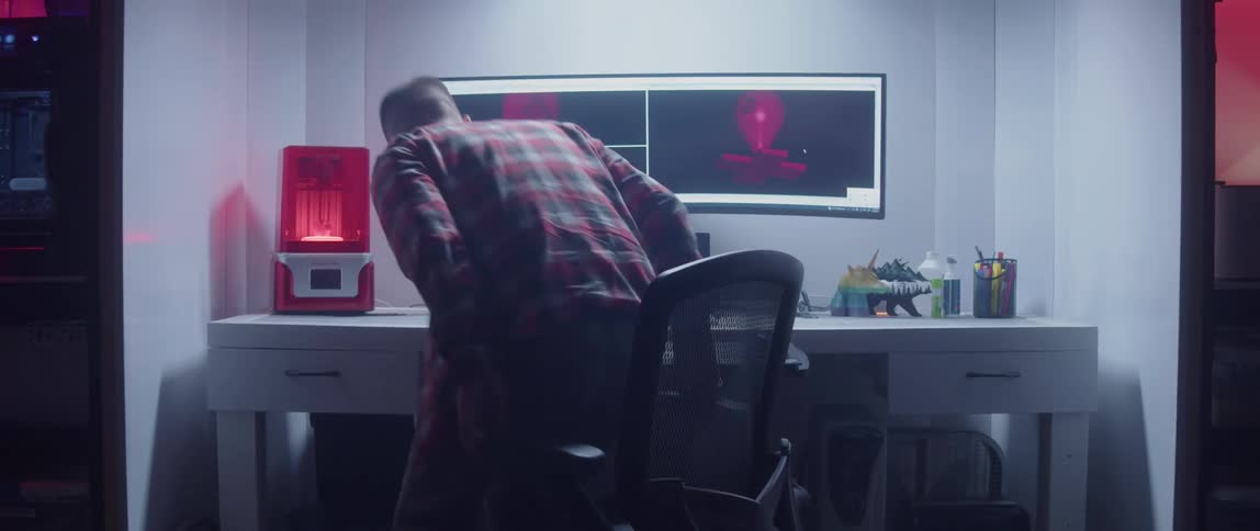 A man sitting down at an office desk with a widescreen monitor