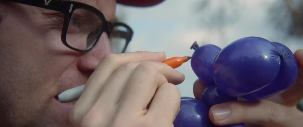 A young man is drawing on a balloon outdoors in the middle of the day