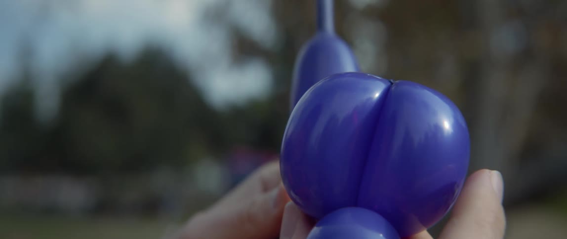Someone is outside twisting a blue balloon into an animal with their hands