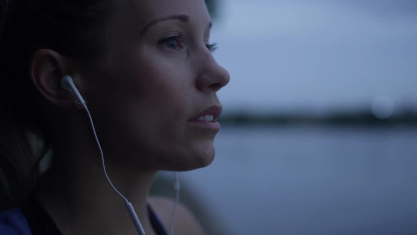 A woman wearing earbuds stares off into the distance