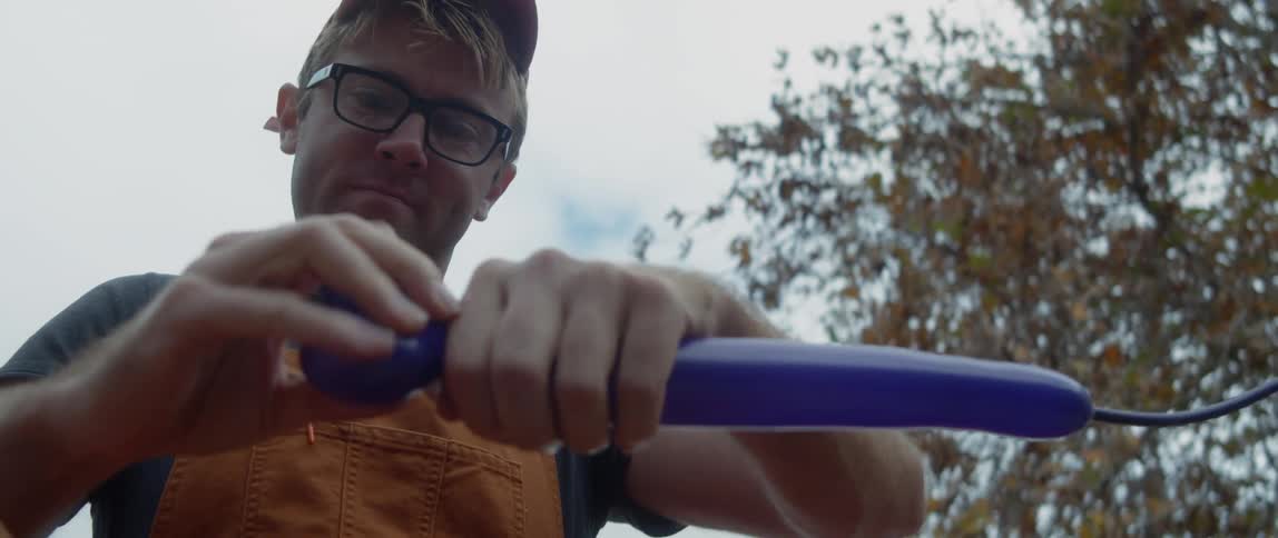 A man is standing outside twisting a blue balloon into an animal with his hands