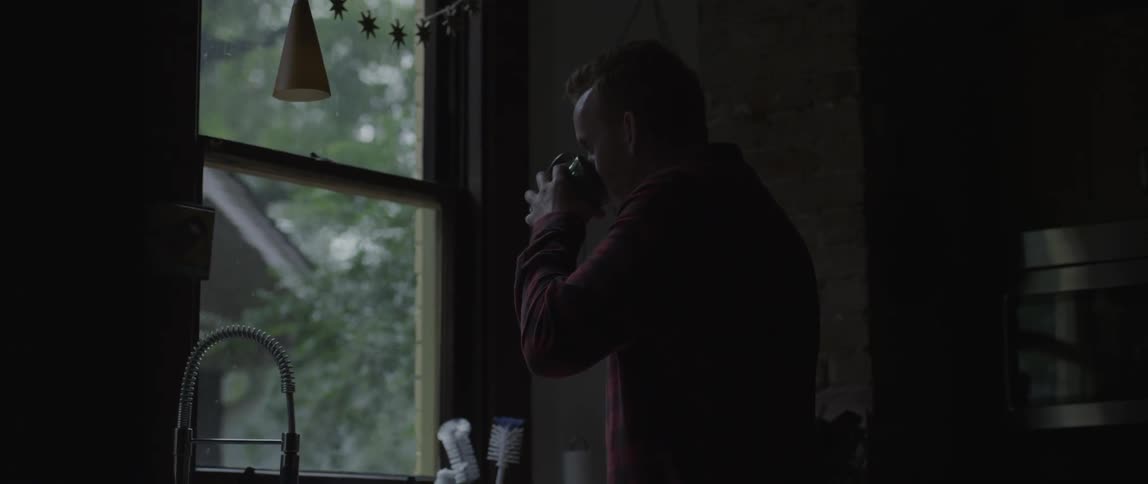 A man drinks from his mug watching the rain outside