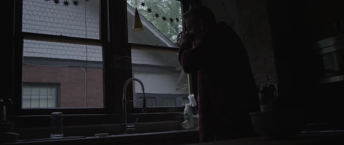 A man drinks from his mug by a window