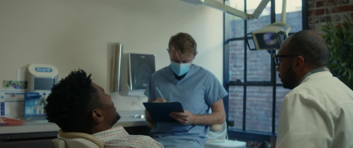 A dentist speaks with a patient while a colleague takes notes