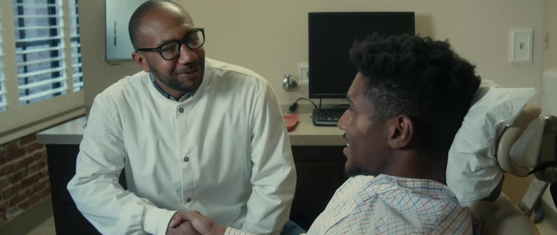 A man is sitting in a chair at a dental clinic and shaking hands with the dentist