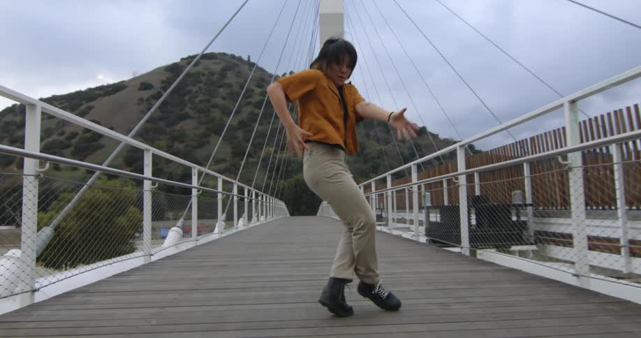 Young performer dances fluidly walking forward over a suspension bridge