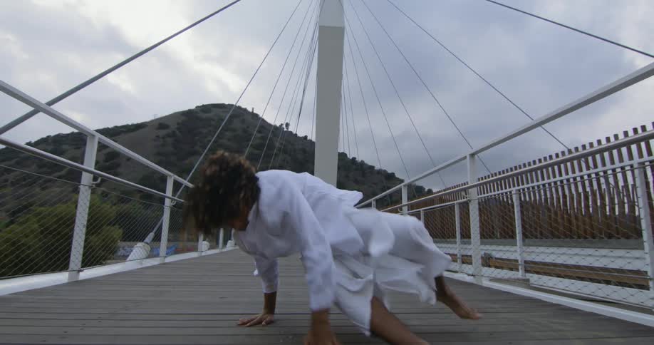 Young performer dances fluidly moving forward over a suspension bridge