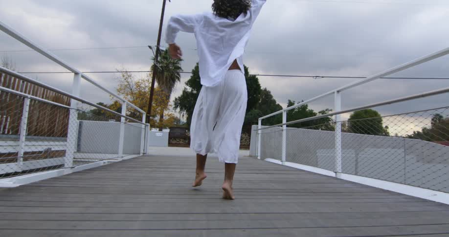 A man is dancing on a bridge during dusk