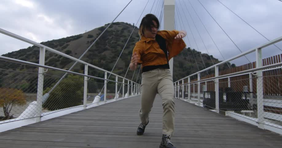 Young performer dances fluidly walking forward over a suspension bridge