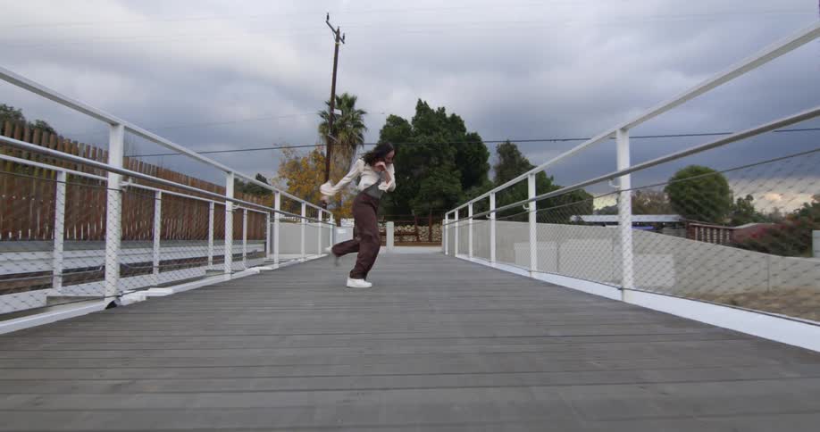 A young white woman is dancing around on a bridge in the day time