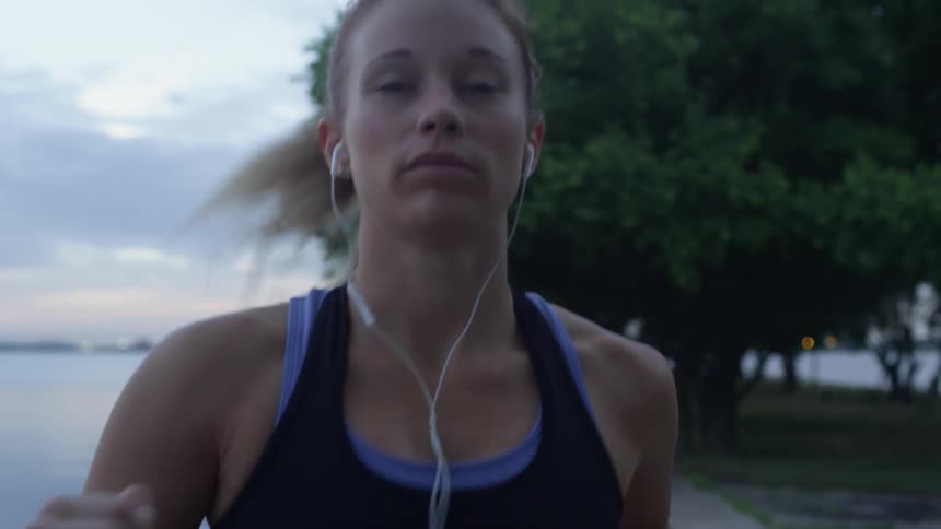 A woman jogs near a lake with earbuds on