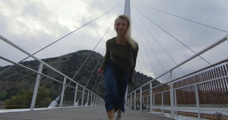Young performer dances fluidly walking forward over a suspension bridge