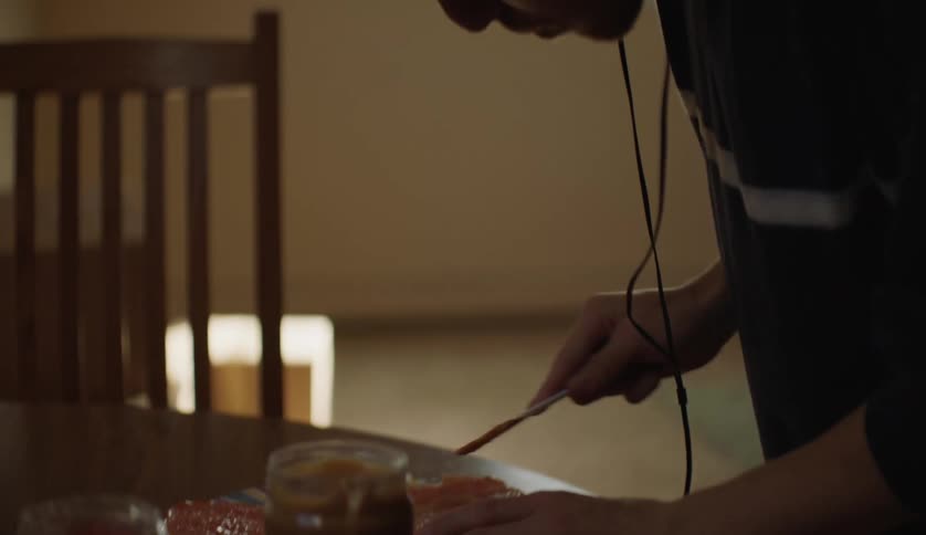 A young man prepares a peanut butter and jelly sandwich in a home kitchen during the day