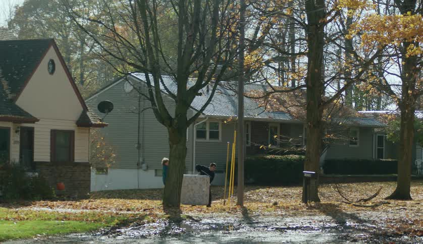 Two people carrying a mattress across the yard in a neighborhood